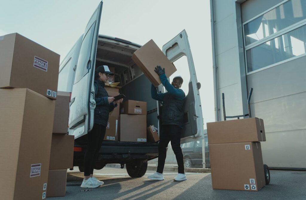 Workers loading boxes into a delivery van at a warehouse facility outdoors.
